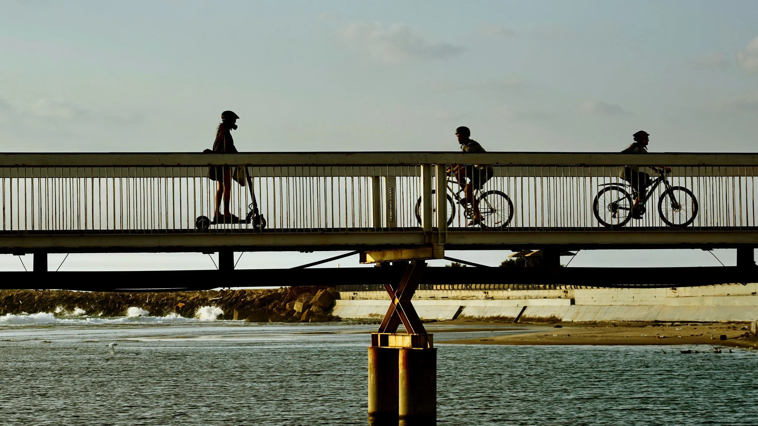 People crossing a footbridge over the seafront at dusk