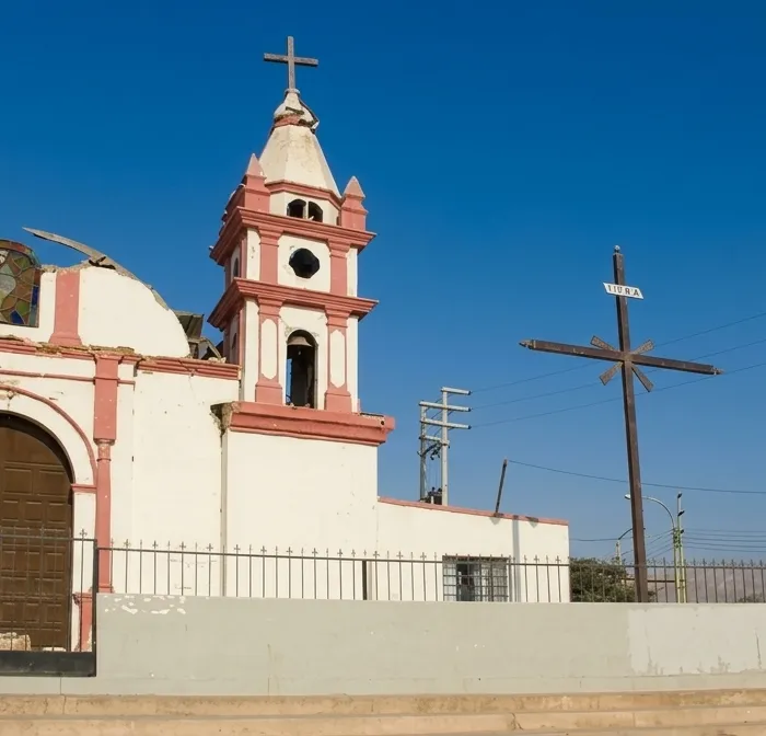La facciata bianca e rosa della chiesa di San José de Los Molinos, con il campanile e una croce di legno sul piazzale