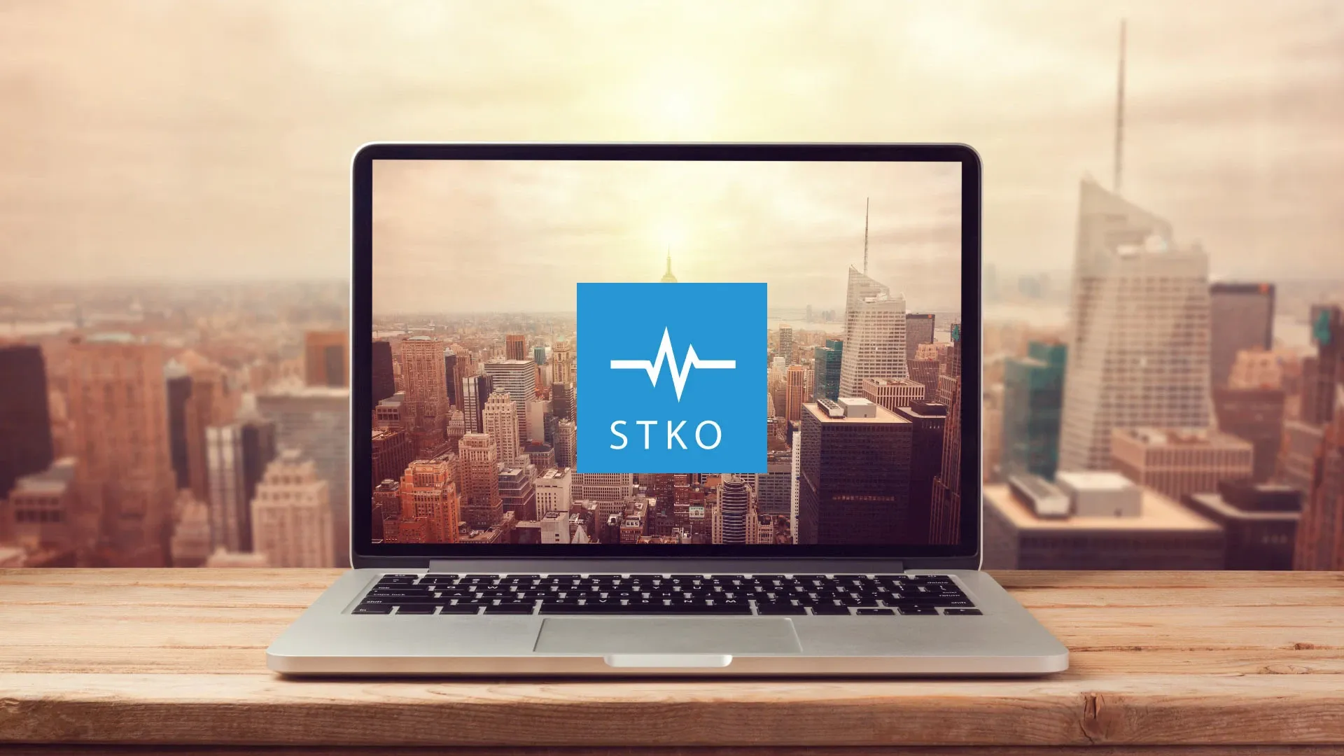 Laptop showing the STKO logo on screen, in front of a city skyline