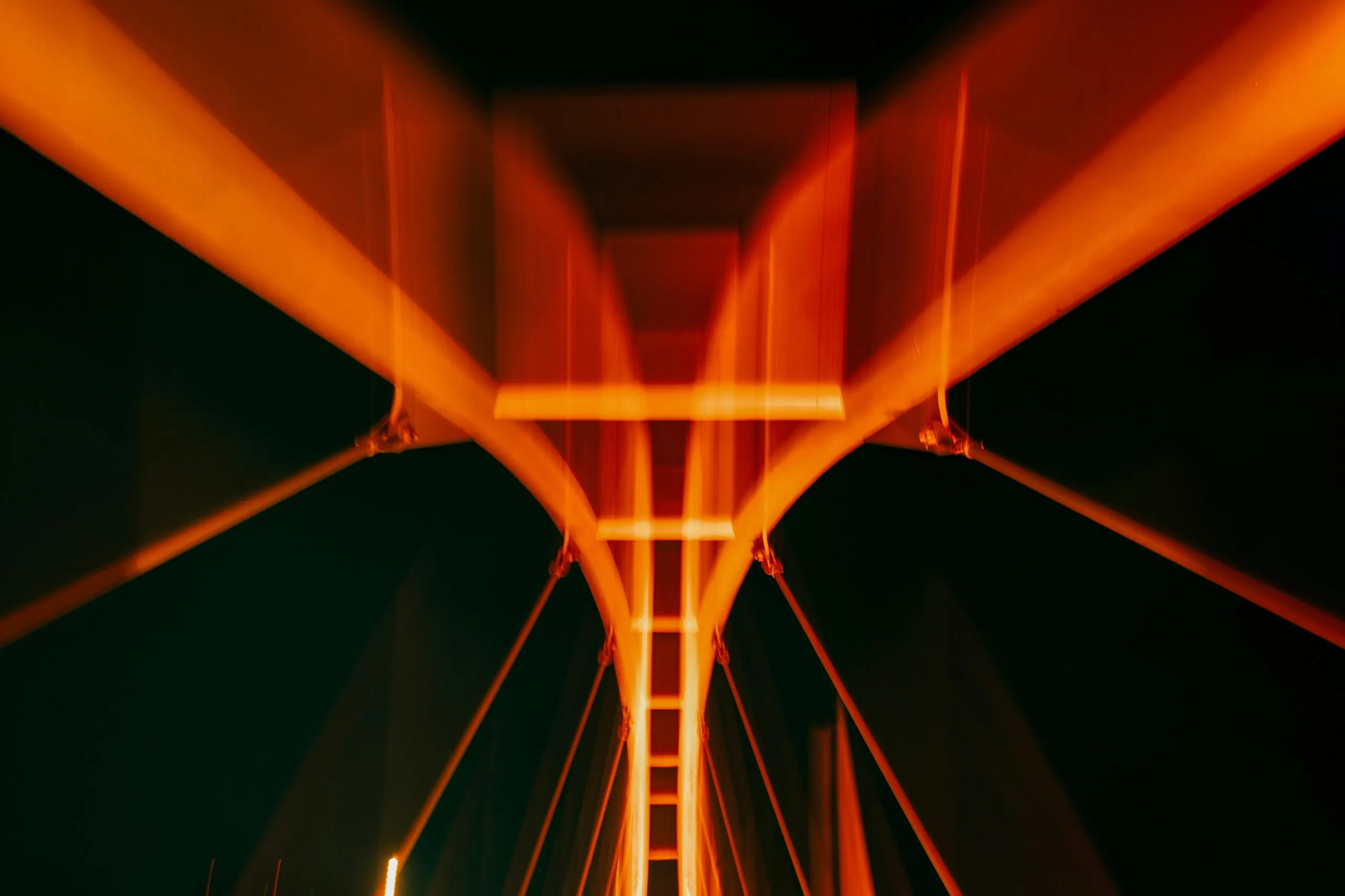 A suspension bridge tower lit orange, seen from below