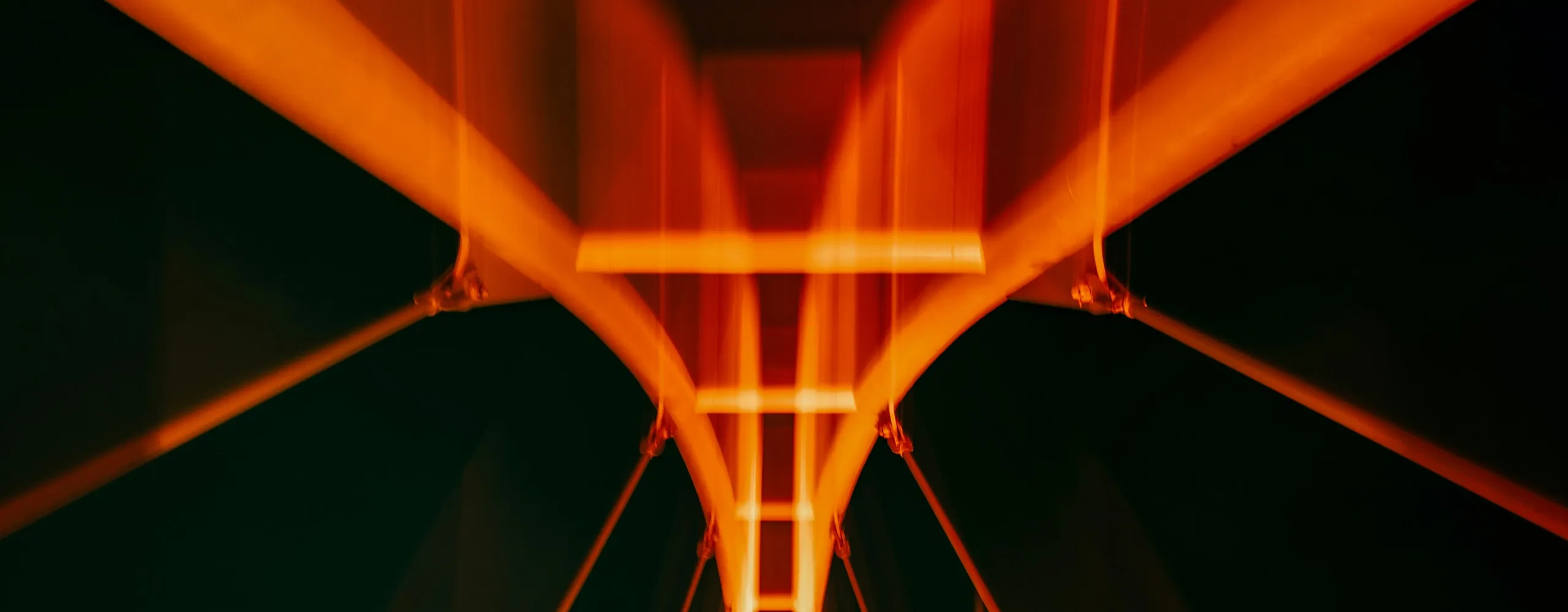 Pilone di un ponte sospeso illuminato di arancione di notte, fotografato dal basso