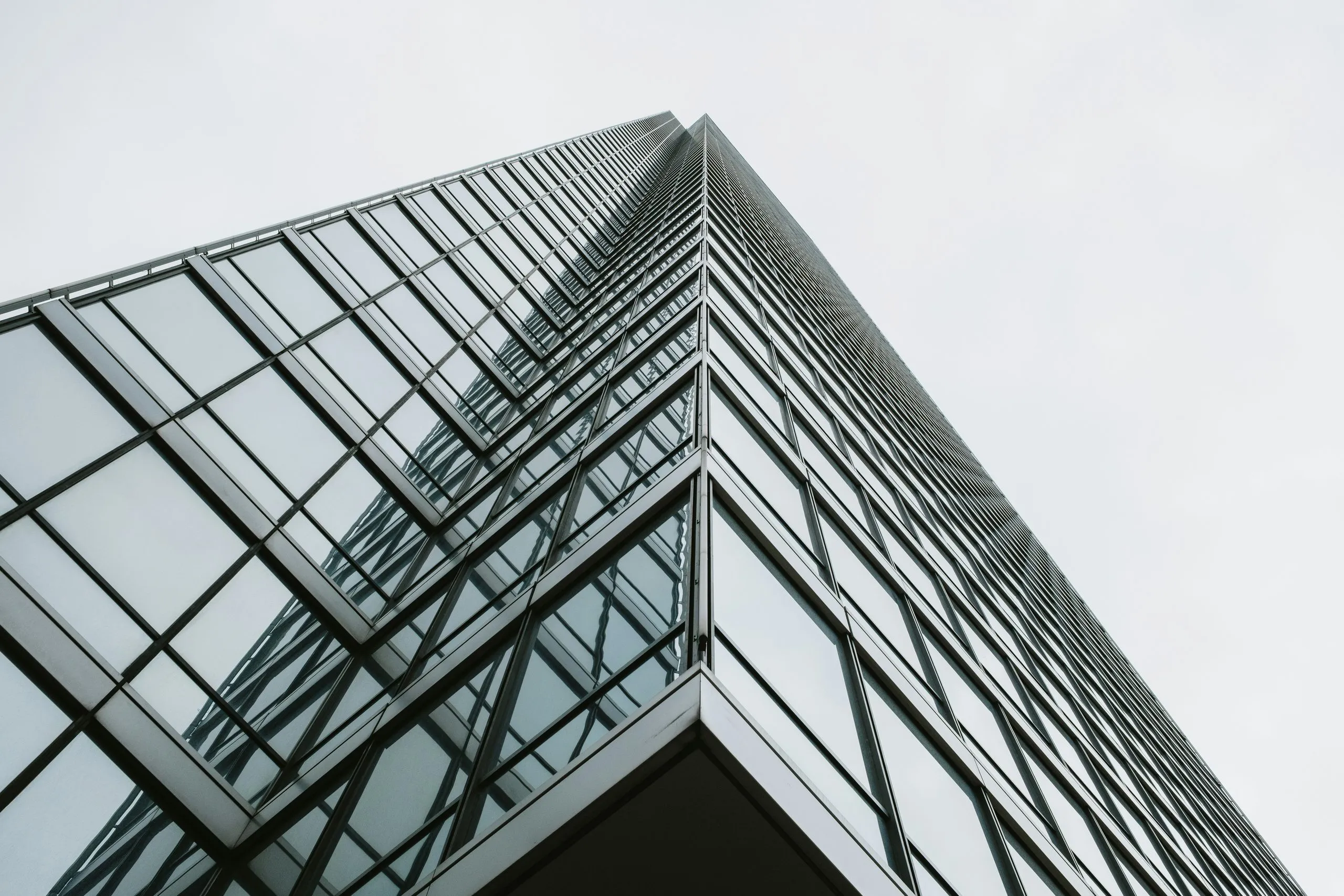 The corner of a glass office tower seen from below against a pale sky
