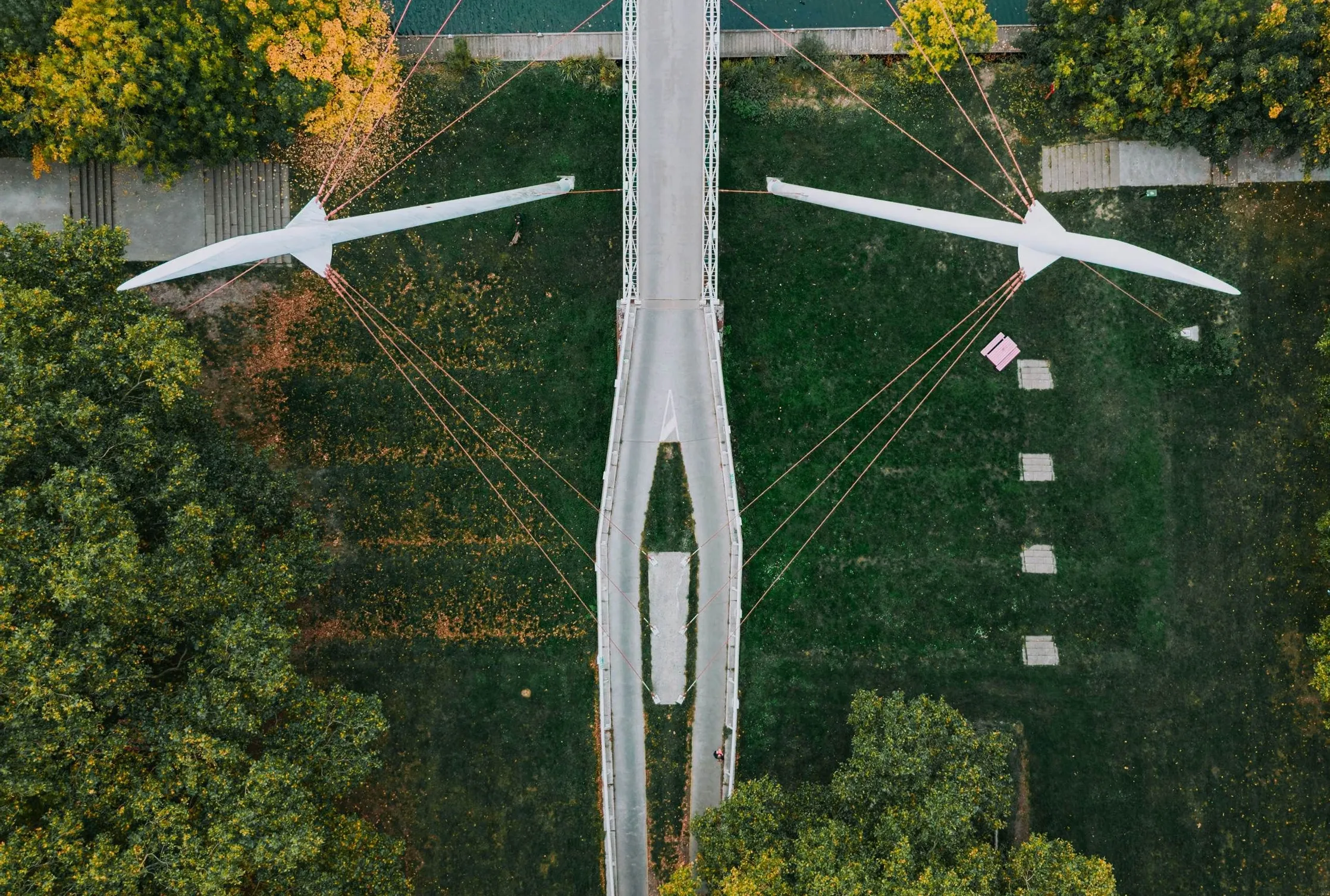 An aerial view of a cable-stayed footbridge crossing parkland