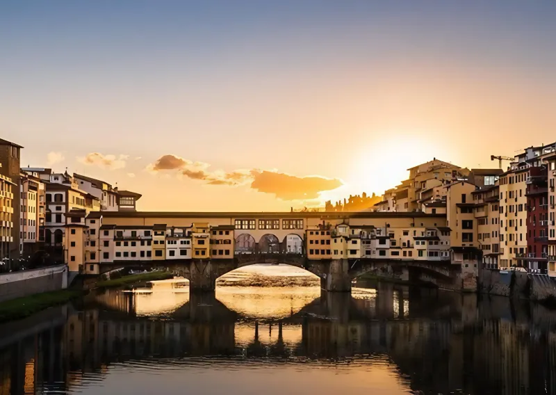 Il Ponte Vecchio di Firenze al tramonto, con le botteghe sospese sull’Arno e i loro riflessi nell’acqua